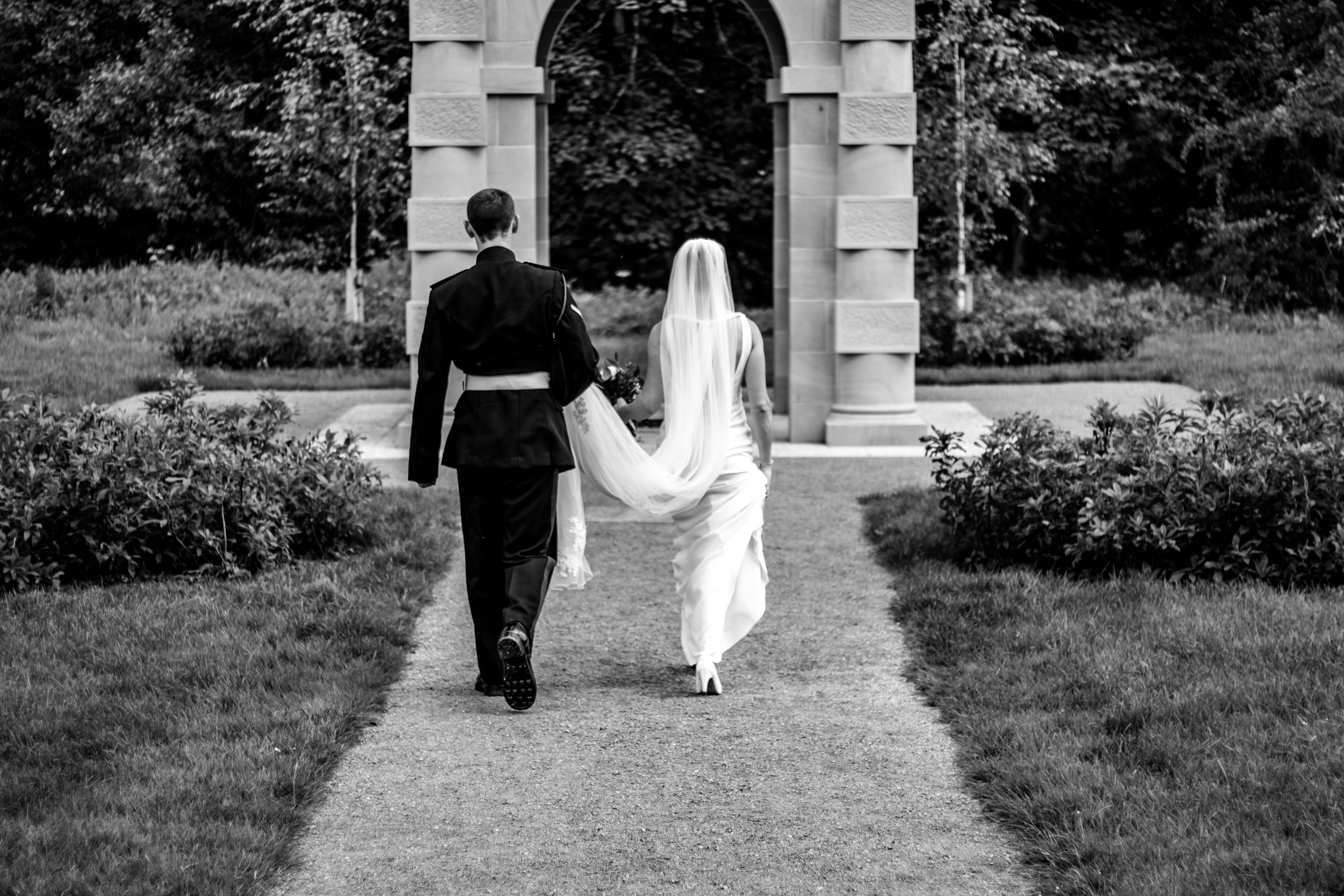 Anna & David — black and white photo of military groom and bride walking towards a stone archway